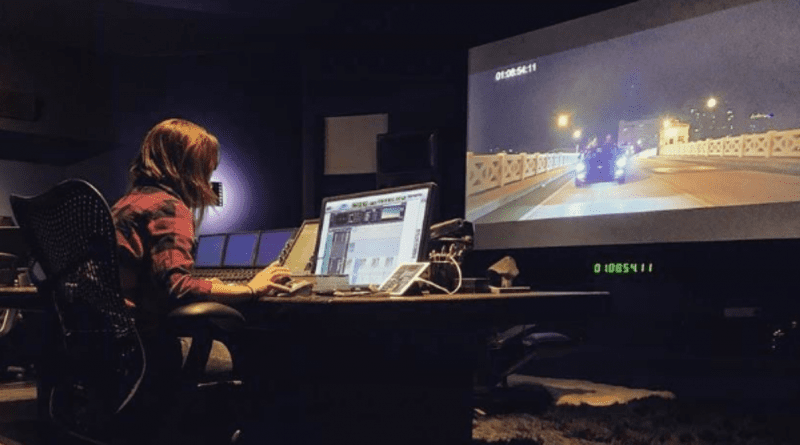 Paola Magrans trabajando en un moderno estudio de sonido frente a una pantalla de televisión gigante.